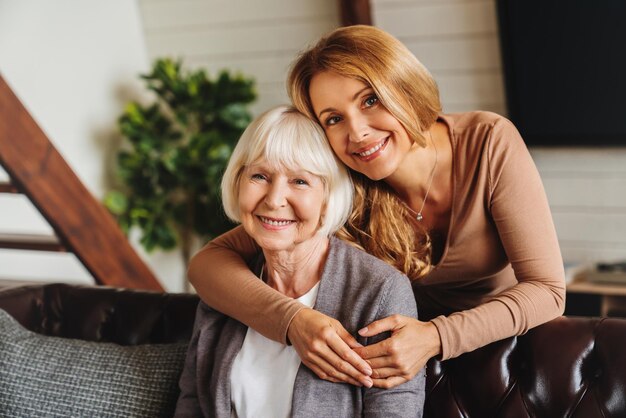 Photo cheerful middle aged woman embracing senior mother at home and looking at camera