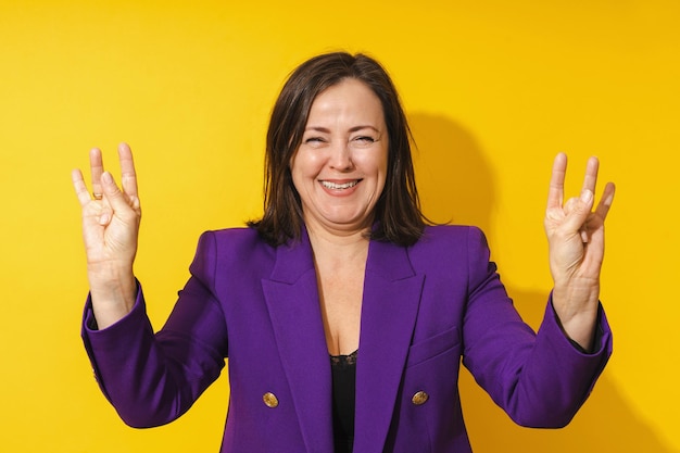 Cheerful middle aged woman showing finger gesture against yellow background