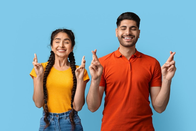 Cheerful middle eastern couple crossing fingers for make a wish