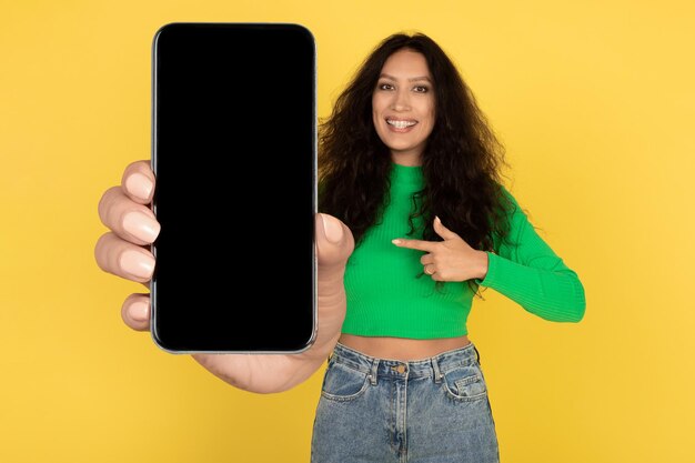 Cheerful middle eastern lady showing big phone screen yellow background