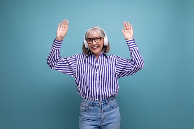 Cheerful middleaged woman with gray hair with headphones listens to music on a bright studio