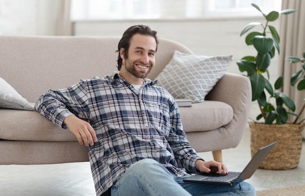 Cheerful millennial european guy with stubble blogger or freelancer in shirt working on laptop in