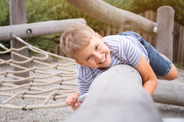 Cheerful and mischievous boy having fun at a wooden playground outdoors.