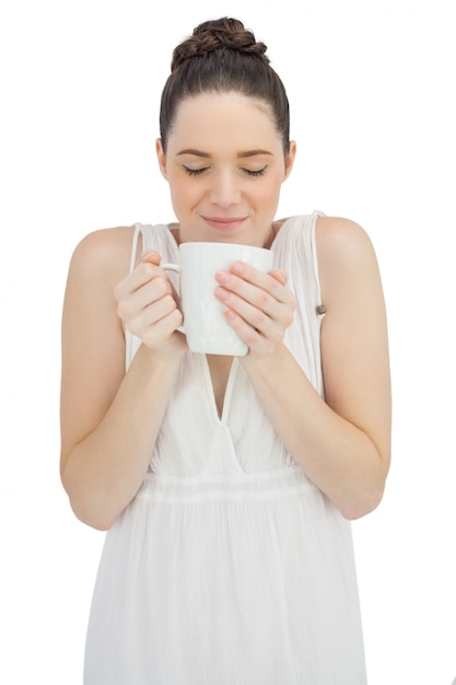 Cheerful model in white dress smelling coffee