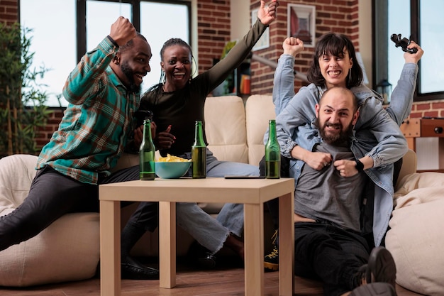 Cheerful modern friends winning video games competition,\
celebrating victory on tv console and having fun with beer bottles.\
group of people feeling happy about game play win at home.