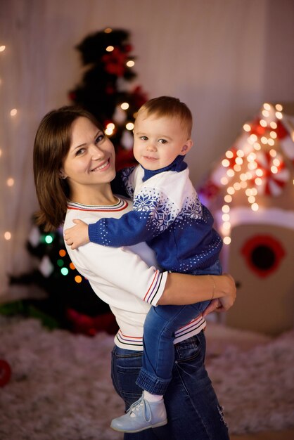 Cheerful mom and her cute son boy having fun near tree indoors