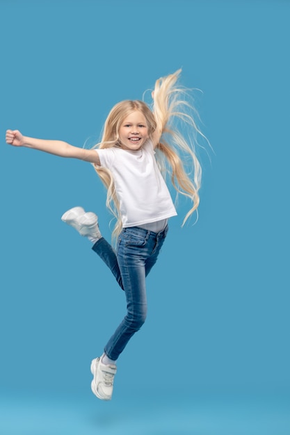 Cheerful mood, jumping. Joyful little girl in tshirt and jeans jumping cheerfully up in photo studio