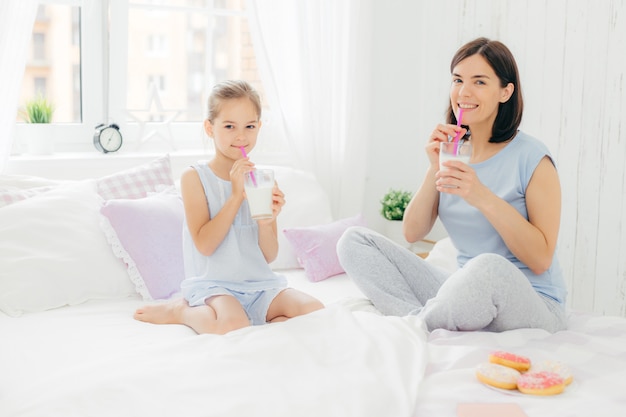 Веселая мама и дочка одеты в пижаму, завтракают по утрам