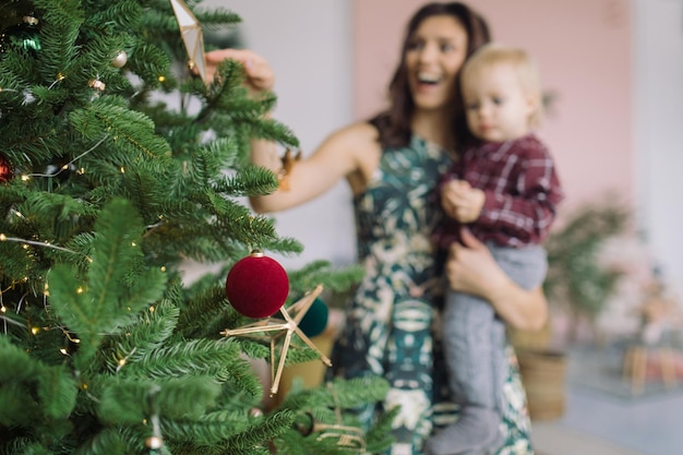 クリスマスツリーが前景で息子を背負っている陽気な母親
