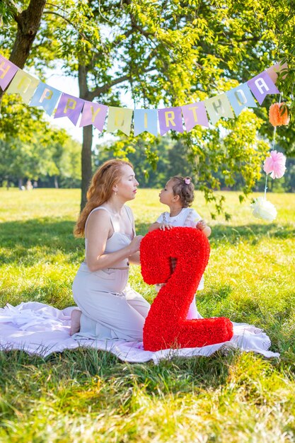 公園で紙の装飾が施された毛布で子供の誕生日を楽しんでいる陽気な母と娘