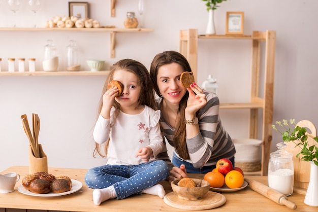 Cheerful mother and daughter in the kitchen preparing Breakfast. They eat cookies, play pancakes and laugh.