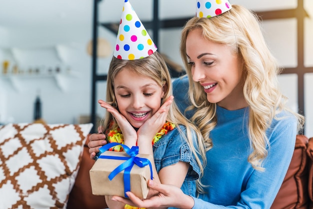 Cheerful mother giving birthday present to her excited daughter at home