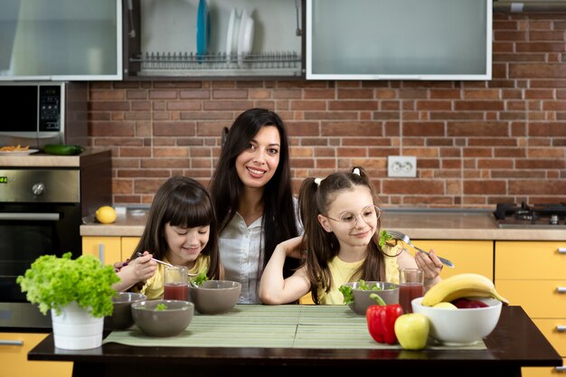 Cheerful mother and two daughters are eating healthy salad together at home. The concept of healthy eating, family values, time together