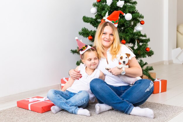 Cheerful mother with her daughter and jack russell terrier dog sitting near the Christmas tree