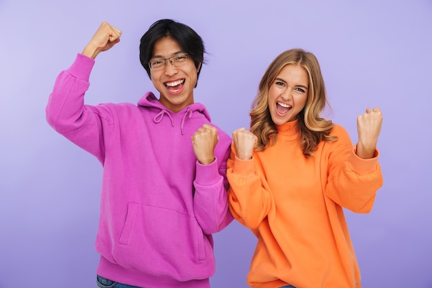 Cheerful multhiethnic teenage couple standing together isolated, celebrating