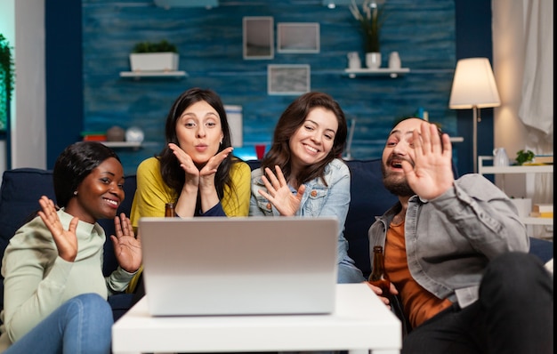 Cheerful multi ethnic friends waving at camera during online internet video call conference while having fun. Group of multiracial people spending time together sitting on couch