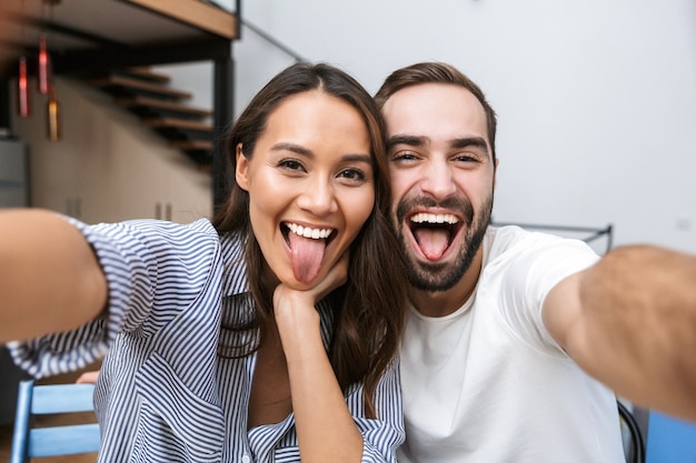 Cheerful multiethnic couple taking a selfie while sitting at the kitchen