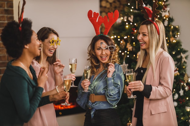 Cheerful multiethnic girls having fun while toasting with champagne on Christmas or New Year's home party together.