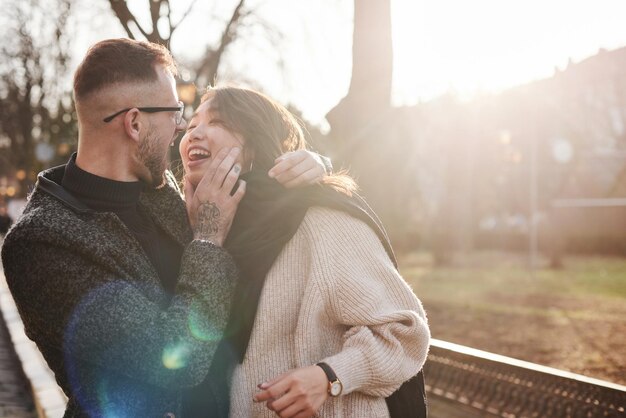 Cheerful multiracial couple embracing each other outdoors in the city. Asian girl with her caucasian boyfriend.