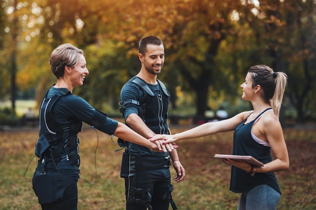 Cheerful muscular couple, dressed EMS vests, are successfully finished training with personal trainer in the park.