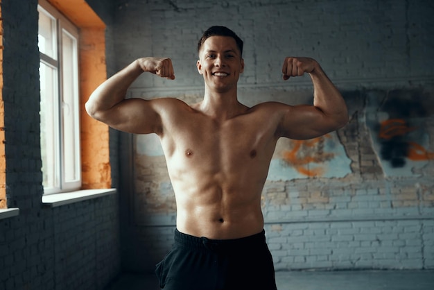 Photo cheerful muscular man showing his perfect biceps while standing in gym