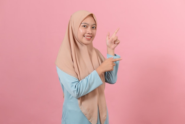 Cheerful muslim woman pointing at copy space on pink background