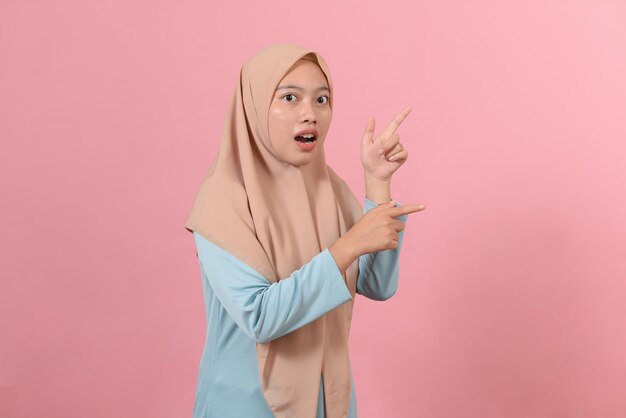 Cheerful muslim woman pointing at copy space on pink background