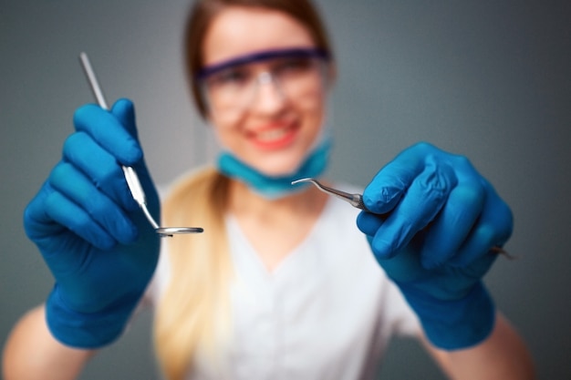 Cheerful nice young woman dentist look on camera and smile. She hold dental tools. Isolated on green .