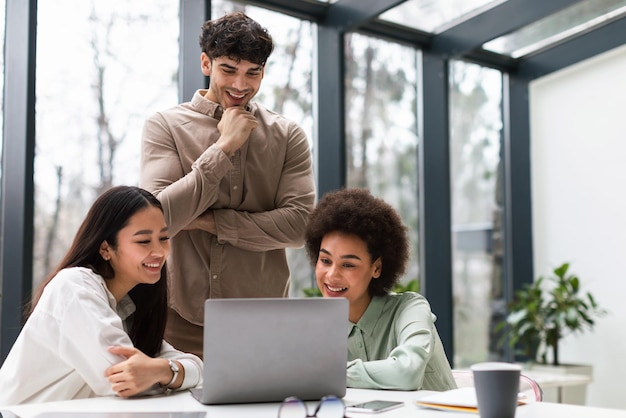 Cheerful office workers trio looking at laptop discussing work indoor