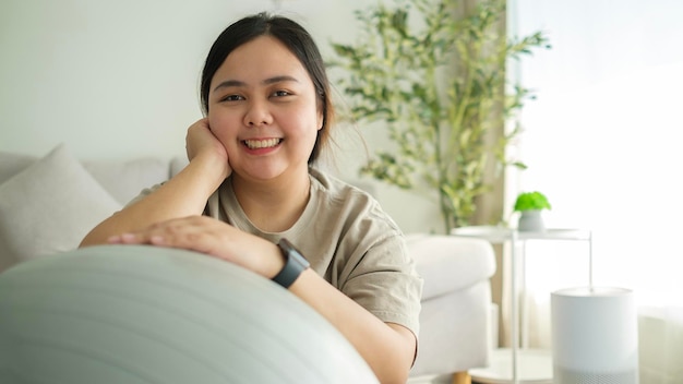 写真 cheerful overweight young woman with exercise ball sitting on yoga mat at home healthy lifestyle concept