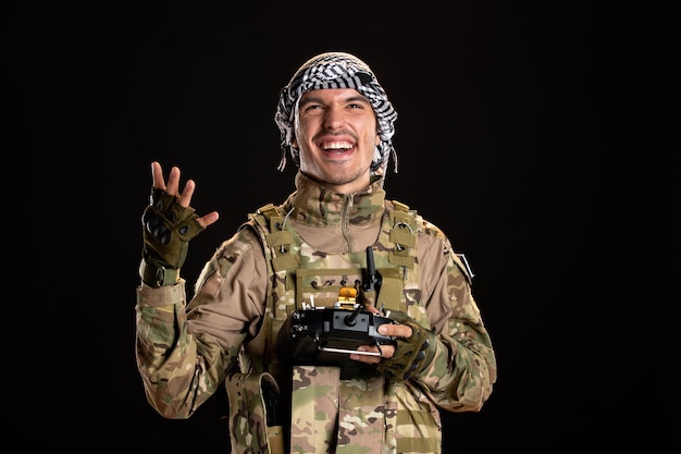 Cheerful palestinian soldier using remote controller on black wall 