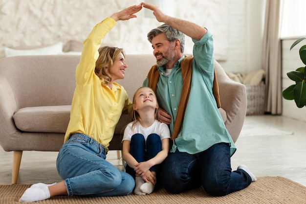 Cheerful parents joining arms making symbolic roof above daughter indoor