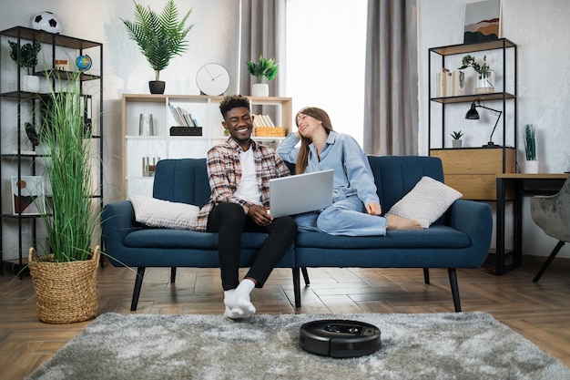 Cheerful people resting on couch while robot cleaning house