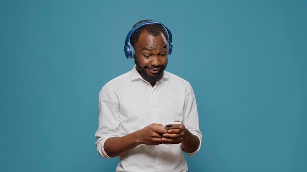 Cheerful person listening to music on headphones and using smartphone, enjoying mp3 stereo sound and browsing internet on mobile phone. Happy man having fun with audio headset.