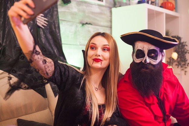 Foto allegra donna pirata e vampiro alla festa di halloween che si fa un selfie.