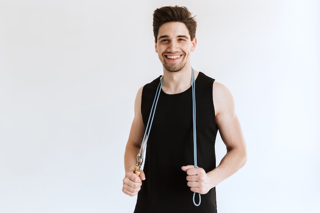 cheerful pleased young strong sports man posing and holding skipping rope.