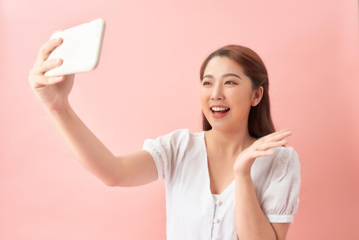 Photo 명랑하고 귀엽고 예쁜 매력적인 여성이 휴가 때 셀카를 찍으며 허리에 손을 얹고 파스텔 색상의 배경에서 소외된 미소를 짓고 있다