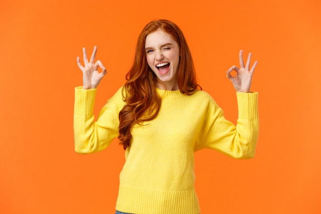 Cheerful and positive, enthusiastic redhead female in yellow sweater winking in approval