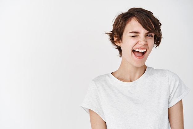 Cheerful and positive natural girl winking , feeling motivated and happy, smiling on white wall