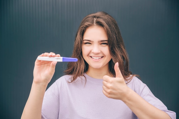 Cheerful positive woman posing on camera with positive pregance test result