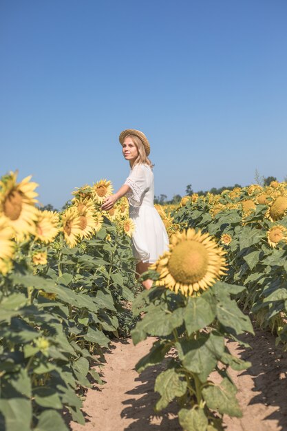 Cheerful positive young woman posing on camera among field of sunflowers Happy girl