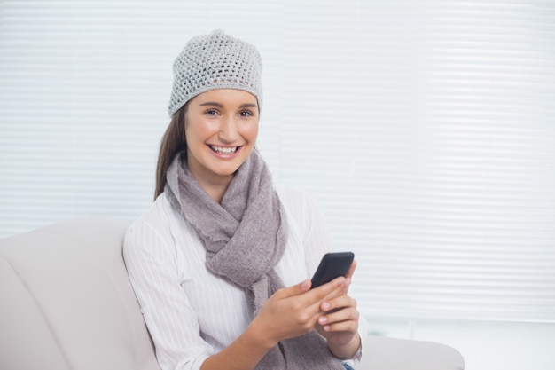 Cheerful pretty brunette with winter hat on holding her phone