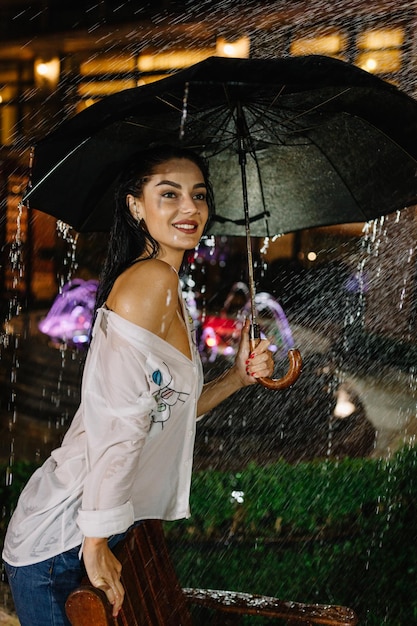 Cheerful pretty girl holding umbrella while strolling outside\
she is turning back and looking at camera with true delight and\
sincere smile copy space in right side