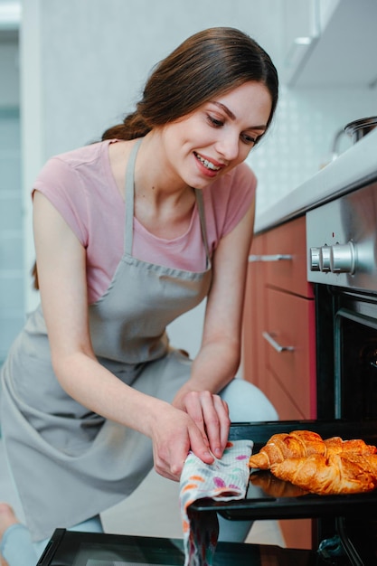 Cheerful pretty lady looking at the pastry on a baking pan with a happy smile