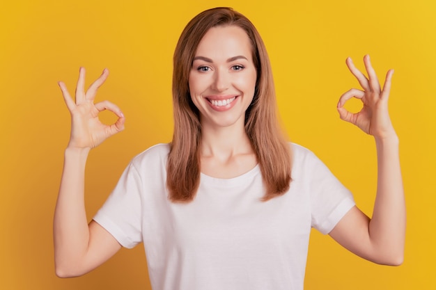 Donna graziosa allegra che mostra il segno ok della mano sorridendo raggiante sul muro giallo