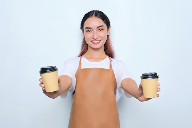 Cheerful pretty young barista girl in apron giving a takeaway cup of coffee isolated on white background