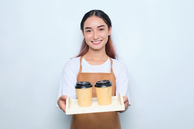 Cheerful pretty young barista girl in apron giving a takeaway cup of coffee isolated on white background