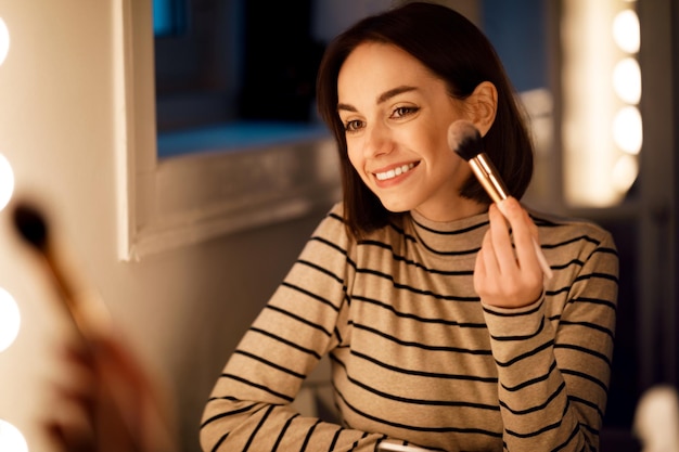 Cheerful pretty young woman applying blush with brush