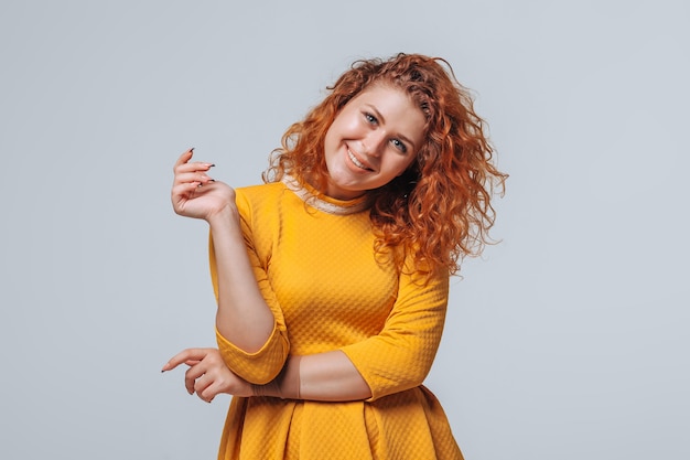 Cheerful red curly girl in a yellow dress on a light gray background