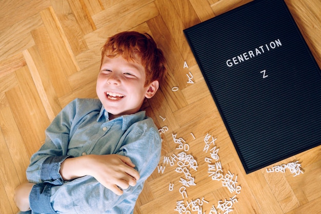 Веселый рыжий маленький мальчик с доской с текстом «Поколение Z»
